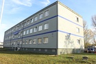 Blick von der Straßenseite auf das Ausbildungszentrum. Man sieht ein großes graues Gebäude mit blauen Akzenten  (Bild anzeigen)